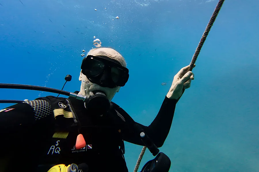 Buzo con máscara sujetando con la mano un cabo tenso bajo el agua.
